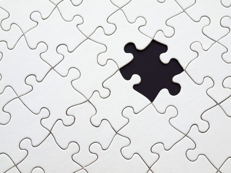 A close-up view of a white jigsaw puzzle with one piece missing, symbolizing how goal setting helps you complete the picture when moving towards your dreams.